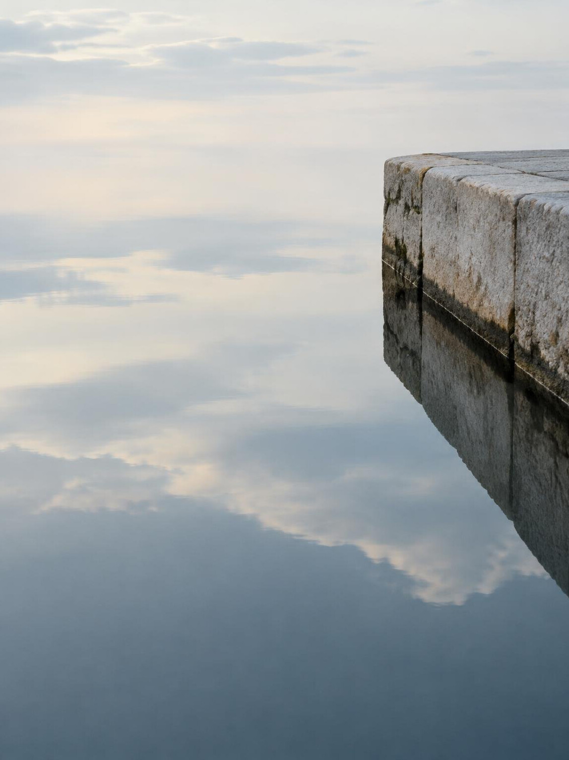 Still water reflecting pale sky and stone